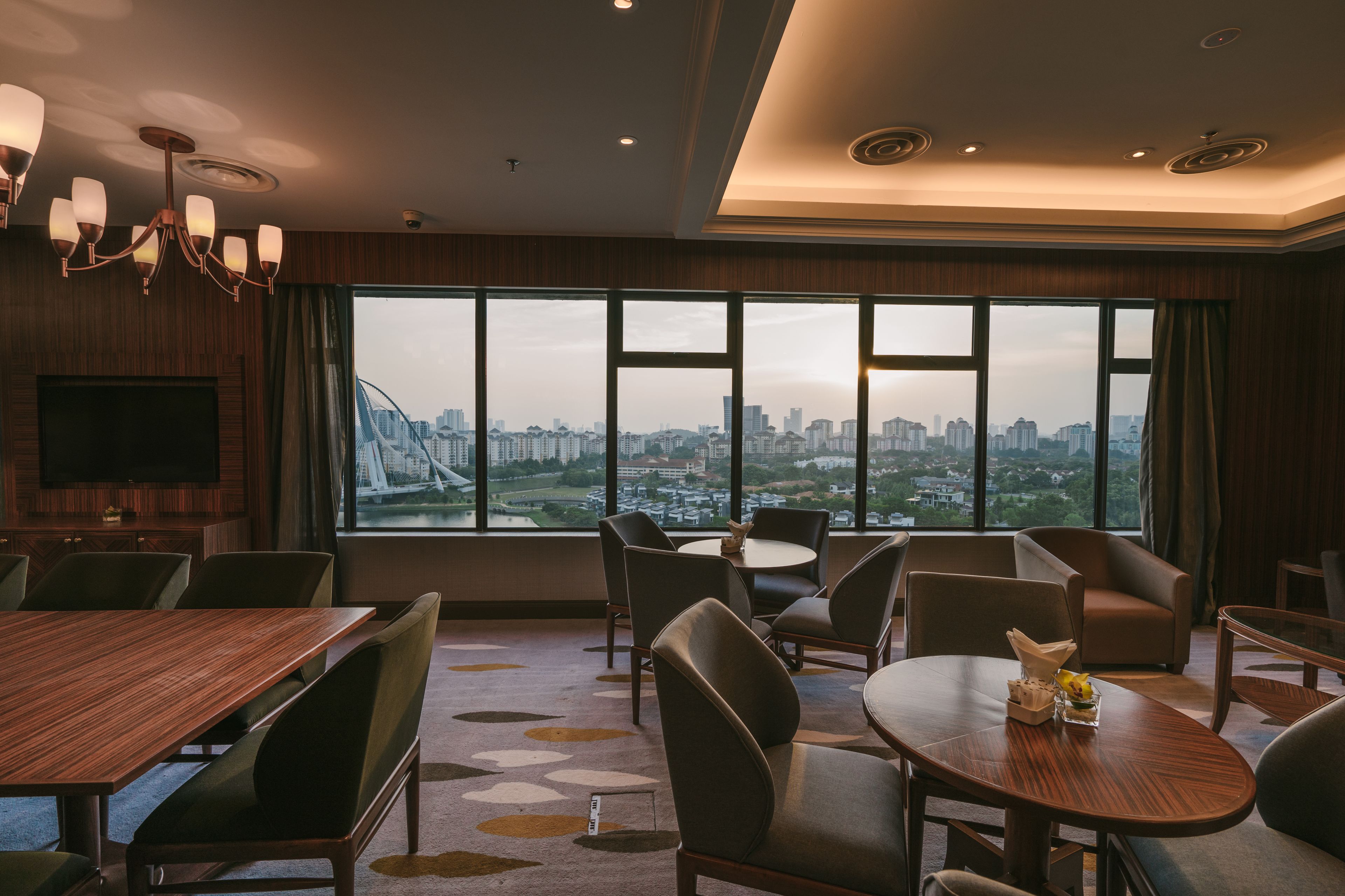 Ein modernes Hotelzimmer mit weitreichendem Stadtblick, einem Essbereich mit Tischen und Stühlen sowie einer Kronleuchter.