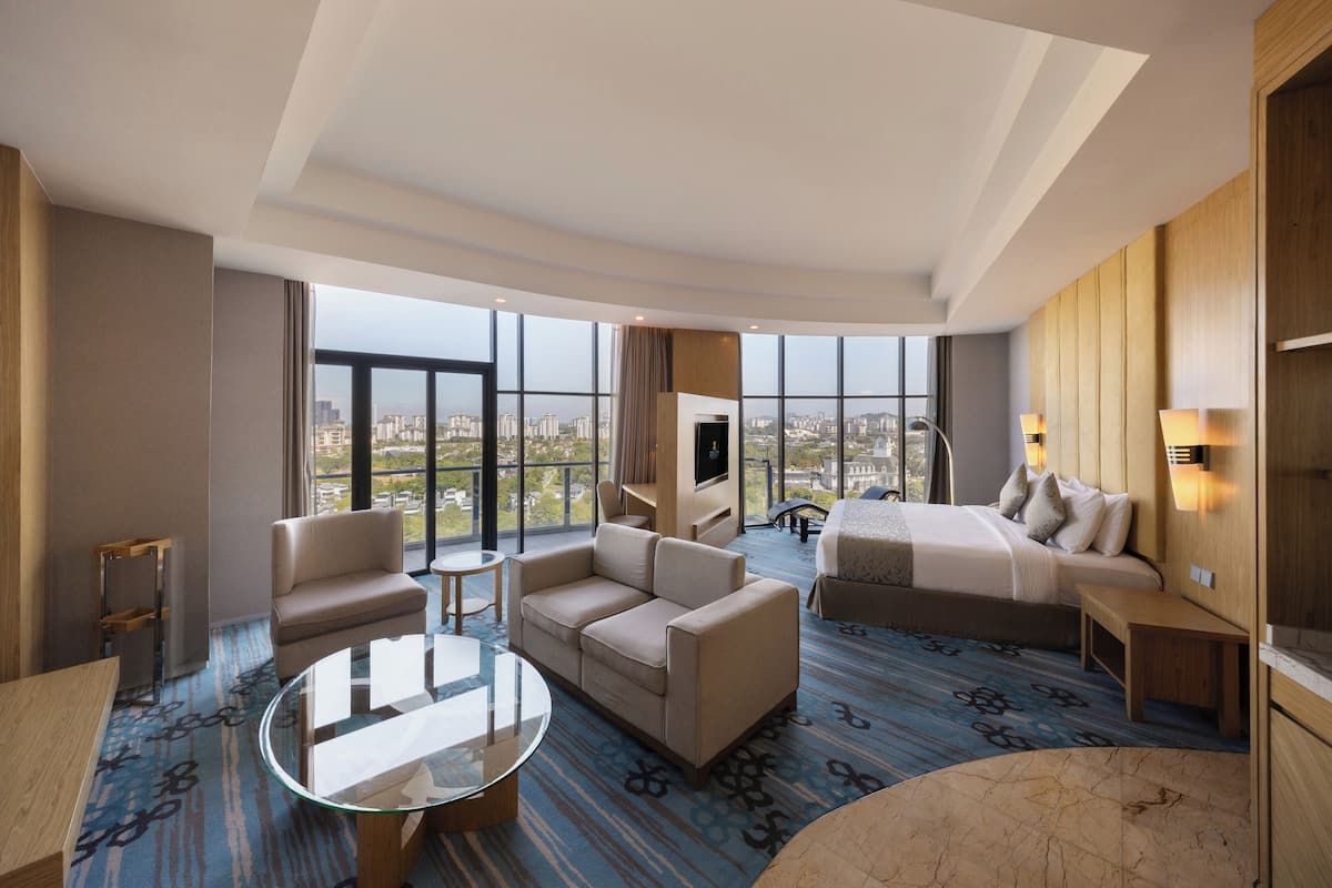 A modern hotel room with a large window, a sofa, a bed, a small table, and a TV.