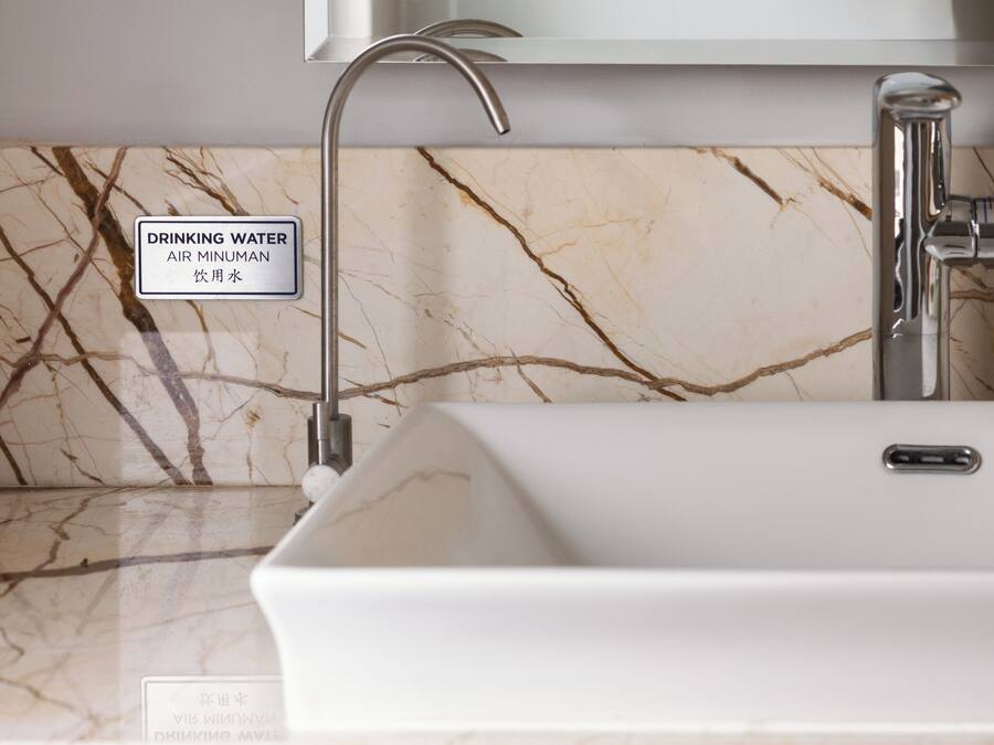 Baño con encimera de mármol, lavabo blanco y grifo. Un letrero indica que el agua es potable.