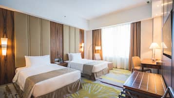 A hotel room with two beds, a desk, a chair, and a large window with curtains.