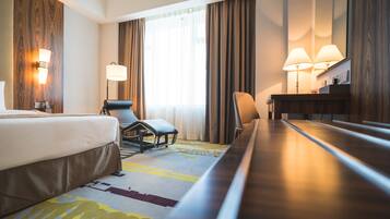 Une chambre d’hôtel avec un lit, deux chaises, un bureau et une grande fenêtre avec des rideaux.
