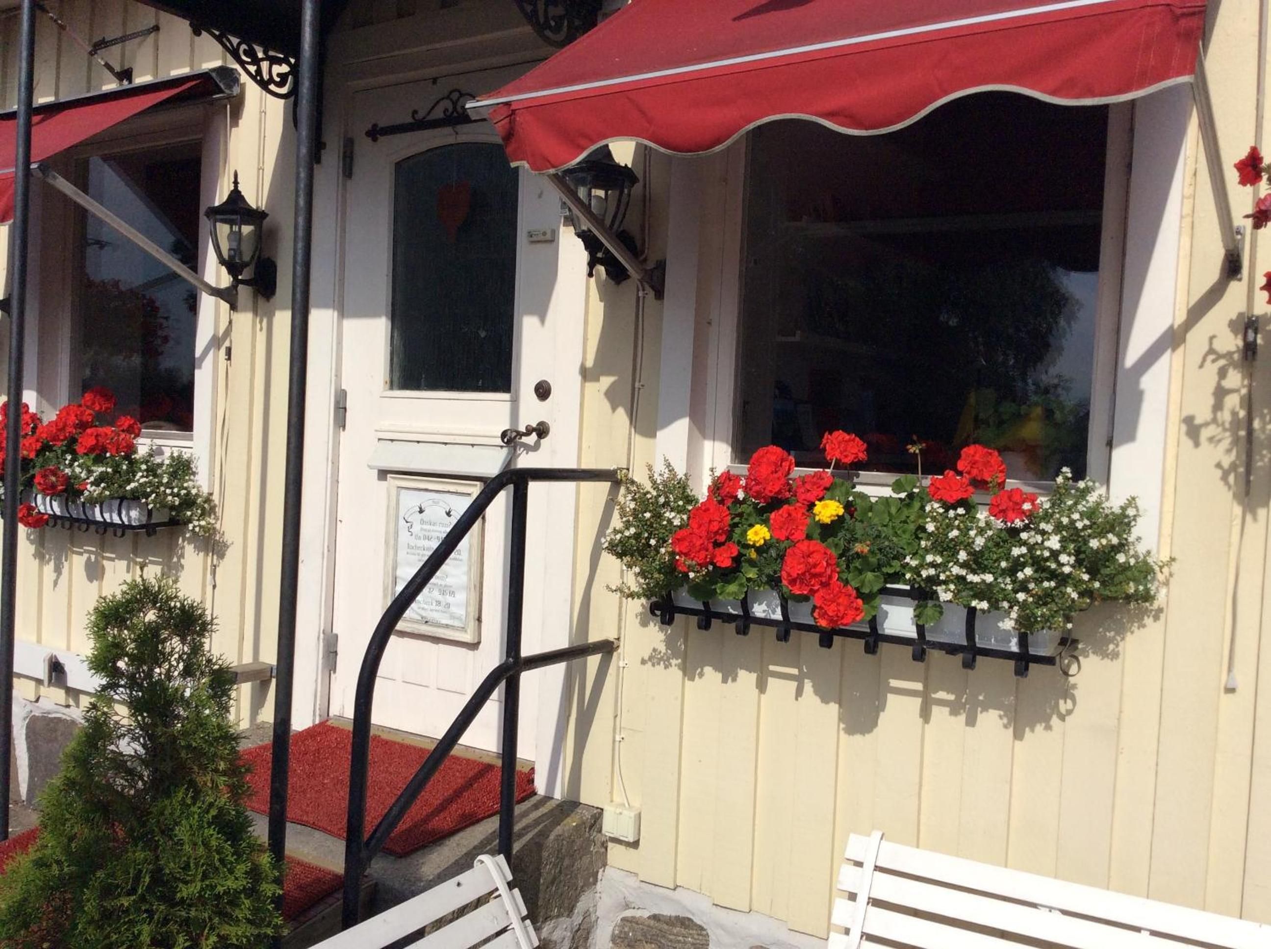 A building with a red awning, a white door, and flower boxes with red flowers.