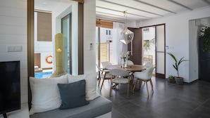 Un salón moderno con sofá, mesa de comedor y sillas. Hay un televisor a la izquierda y un ventanal con vistas al exterior.
