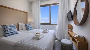 Habitación de hotel con dos camas, televisión, mesita de madera con artículos de aseo y un ventanal grande con cortinas.