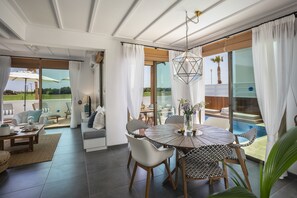 A modern living room with a round dining table, white sofas, and a large sliding glass door leading to a pool area. - Chris Le Mare Luxury Villa By Louis Hotels (Paralimni)