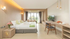 Een hotelkamer met een bed, bureau, televisie en uitzicht op groen.