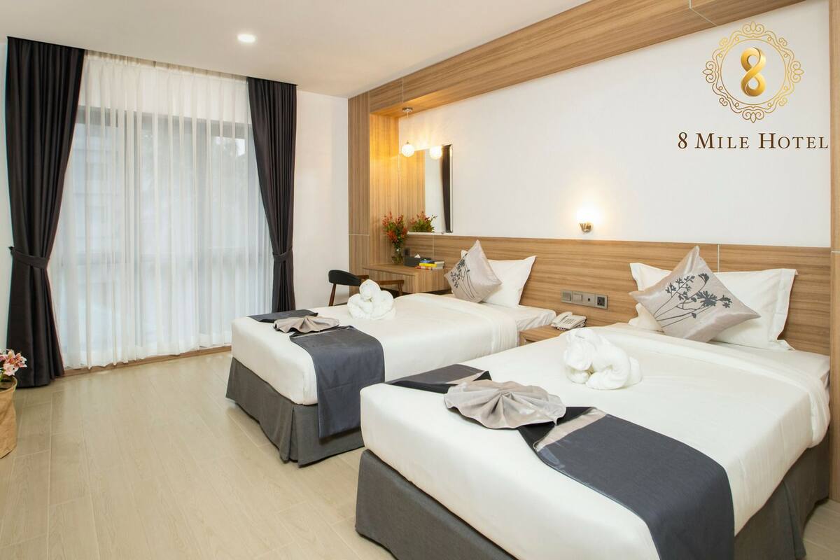 A hotel room with two beds, a TV, a mirror, and a wall-mounted light fixture.