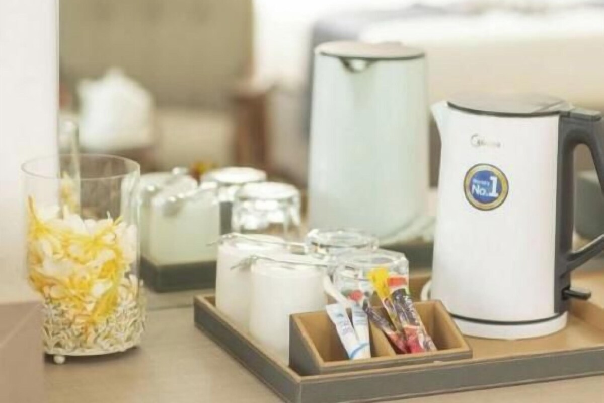 A breakfast setup with a kettle, a glass container with flowers, and a tray with packaged food items.