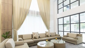 Una sala de estar moderna con un sofá modular, dos mesas de centro redondas y ventanas amplias con cortinas translúcidas.