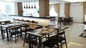 Un comedor moderno con varias mesas y sillas, una barra central y ventanas amplias con cortinas.