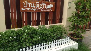 A wooden sign with Thai script and a white fence in front of a building. - Baanmeerak at Ranong (Ranong)