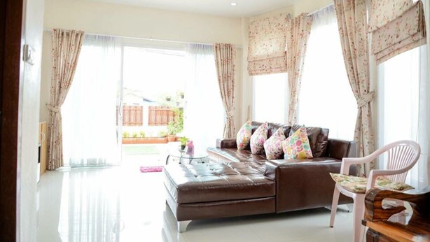 A living room with a brown leather sofa, a pink chair, and floral curtains. - Baanmeerak at Ranong (Ranong)
