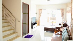 A modern living room with a staircase, a flat-screen TV, a sofa, and a dining area with a table and chairs. - Baanmeerak at Ranong (Ranong)