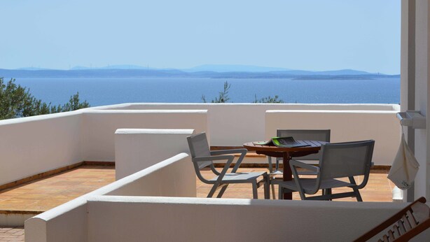 A balcony with a table and chairs, overlooking a body of water and distant land. - Melia Sol Art Studios (Chios)