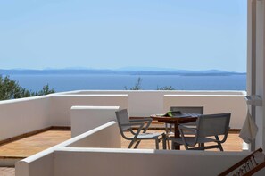 A balcony with a table and chairs, overlooking a body of water and distant land. - Melia Sol Art Studios (Chios)
