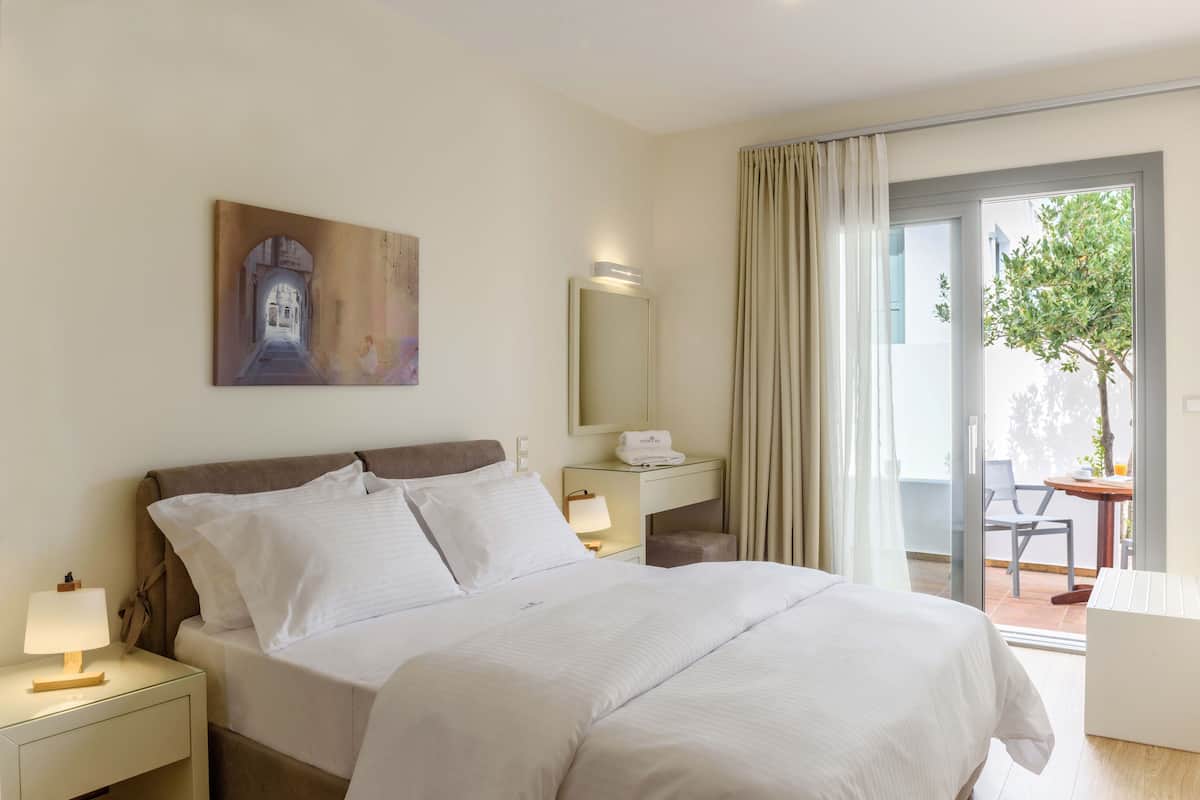 A hotel room with a bed, a nightstand with a lamp, a bedside table with a lamp, a mirror, and a view of the outdoors through a sliding glass door.