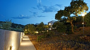 A pathway flanked by a low wall and trees, leading to a building with a modern design. - Melia Sol Art Studios (Chios)