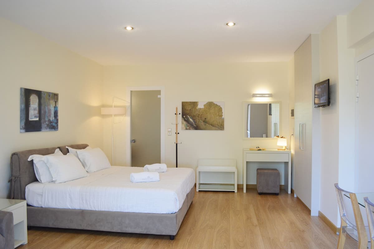 A bedroom with a bed, bedside table, and a desk with a chair. There is a mirror above the desk and a television on the wall.