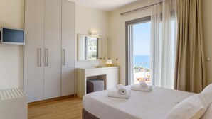 A hotel room with a bed, a TV, a desk, a mirror, and a balcony with curtains. - Melia Sol Art Studios (Chios)