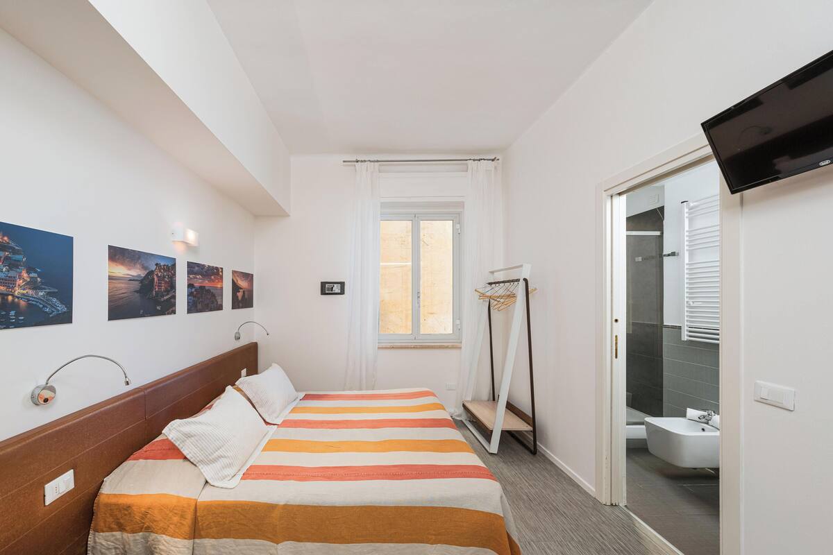 A hotel room with a bed, a TV, a window with curtains, and a view of the sea.