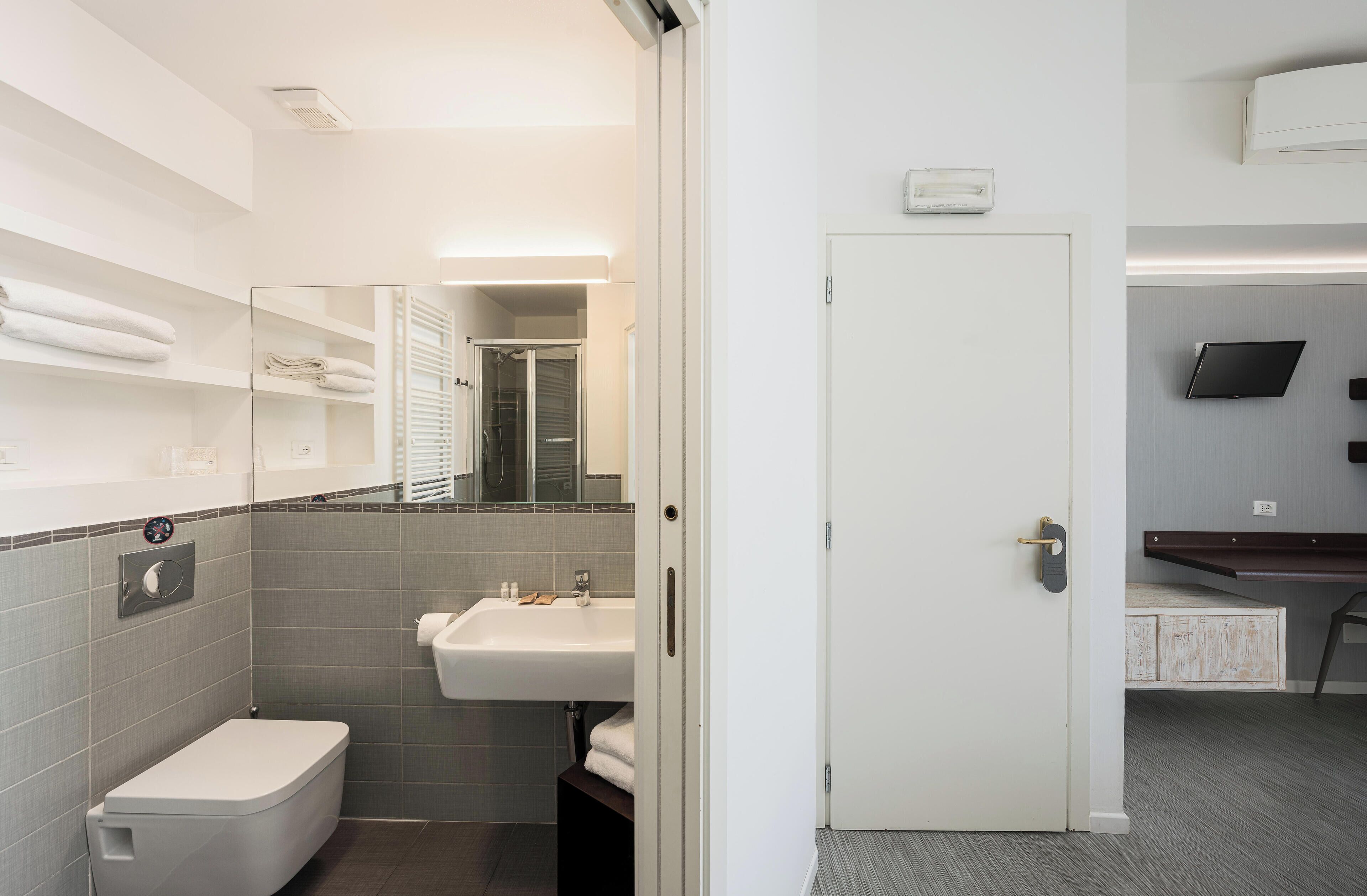 A modern bathroom with a toilet, sink, and mirror. There is a towel rack above the sink and a shower area visible in the background.