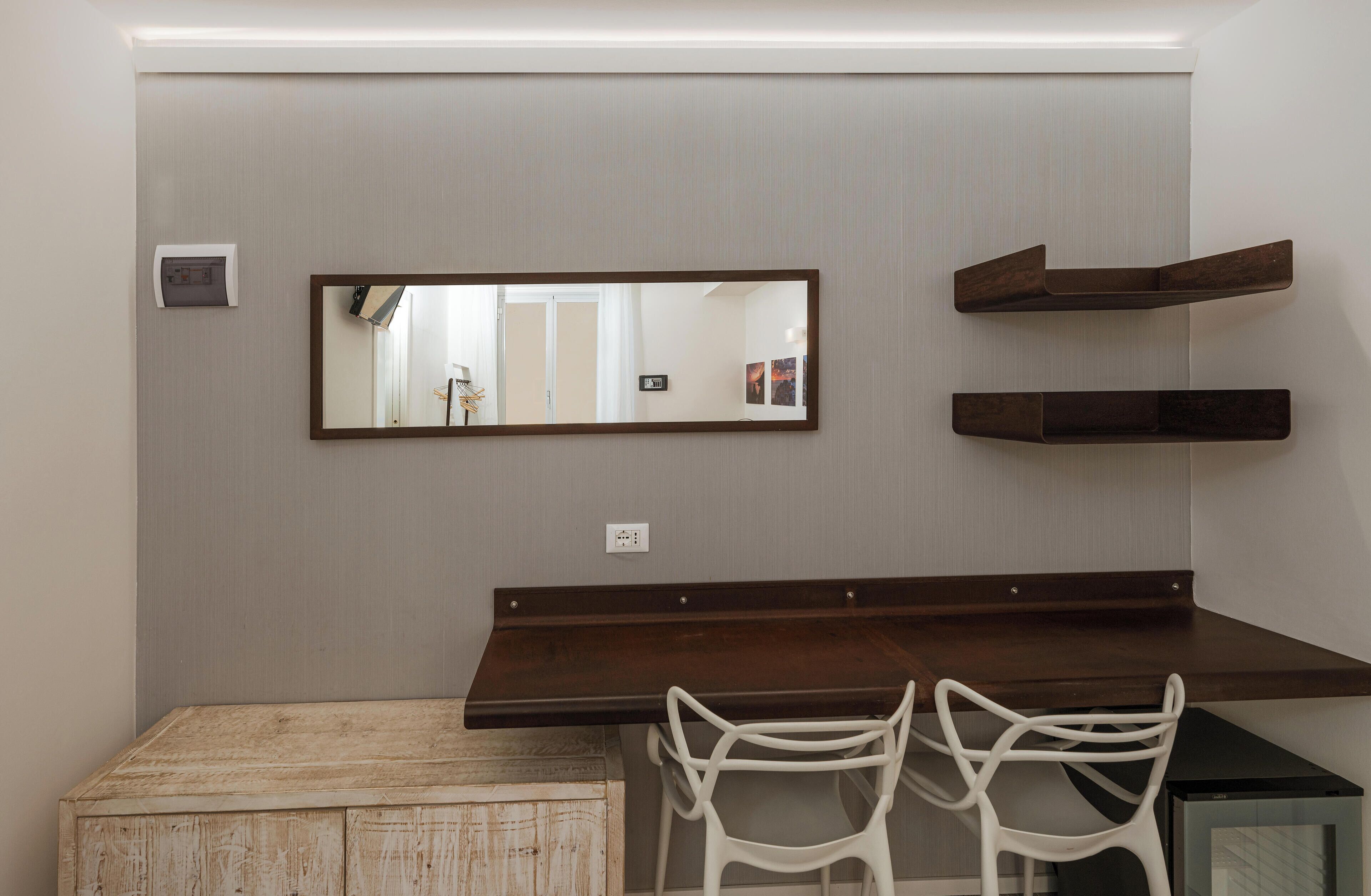 A modern room with a wooden desk, white chairs, a large mirror, and built-in shelves.