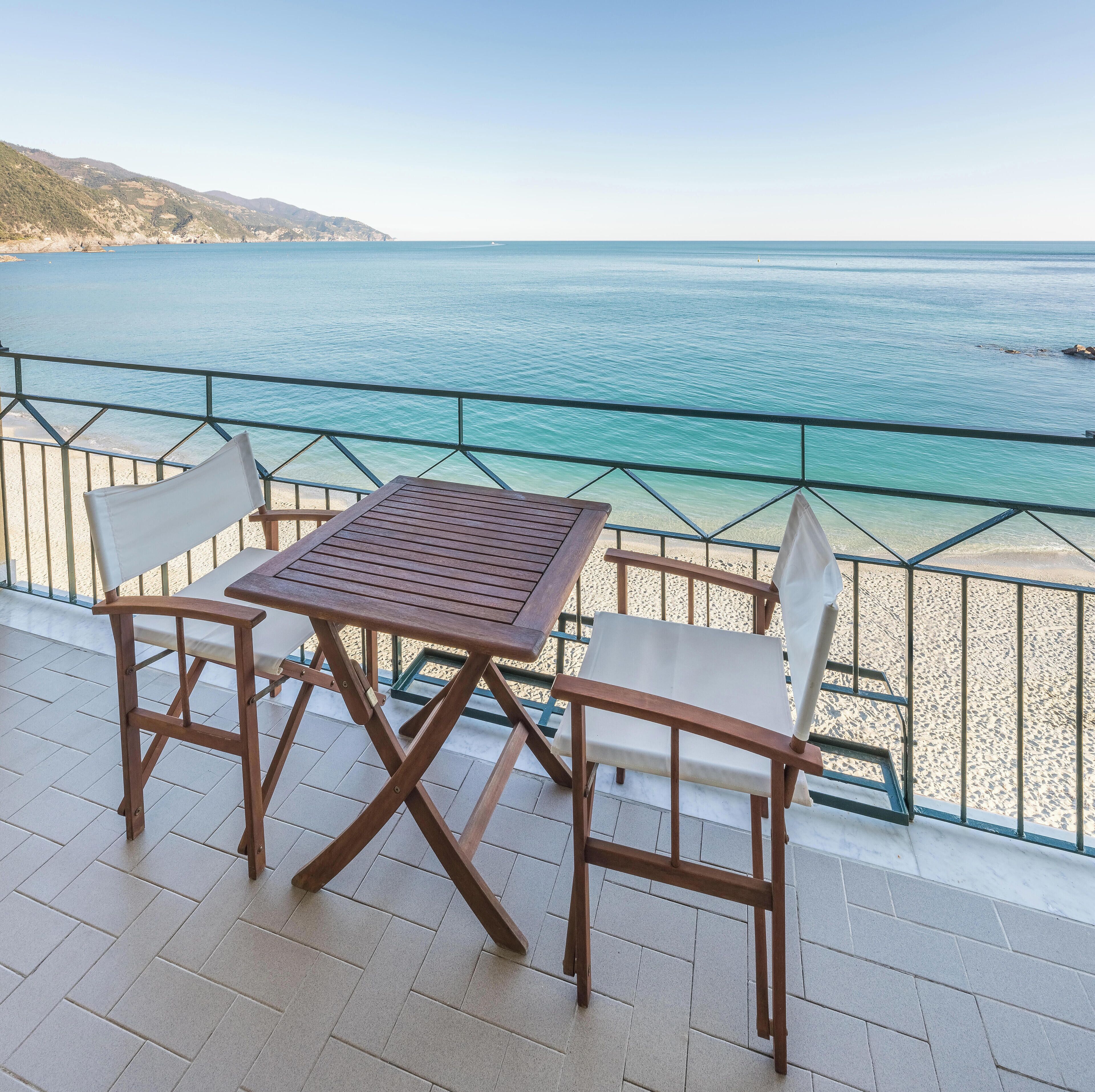 Een houten tafel en twee stoelen op een balkon met uitzicht op zee.