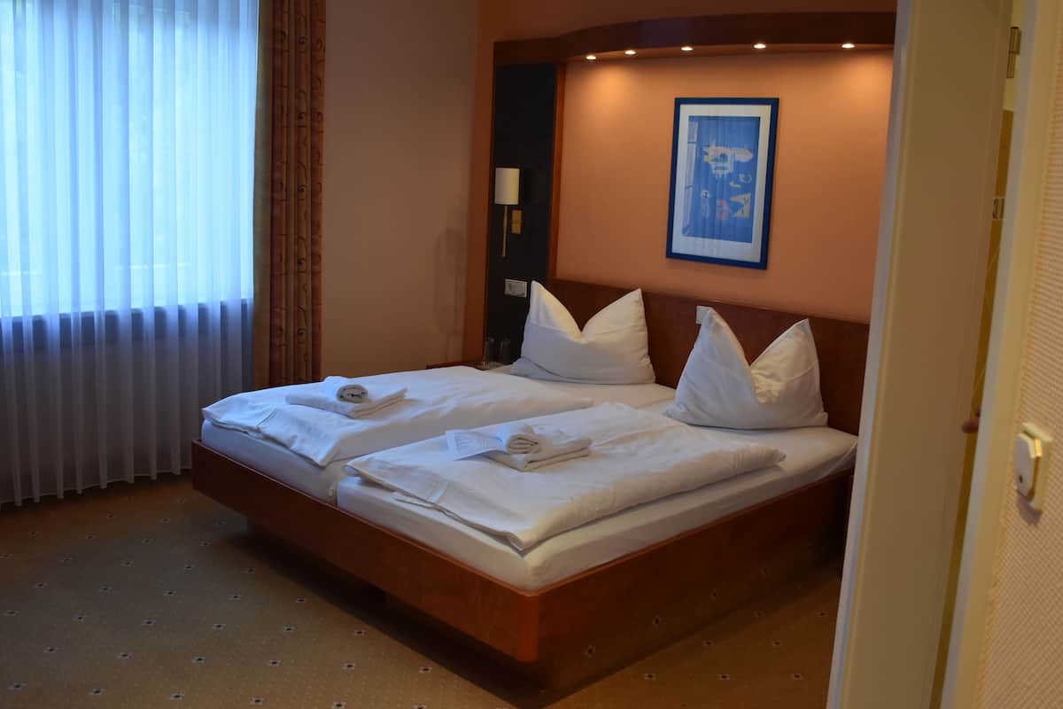 A double bed with white linens and pillows, a bedside table with a lamp, and a framed picture on the wall.