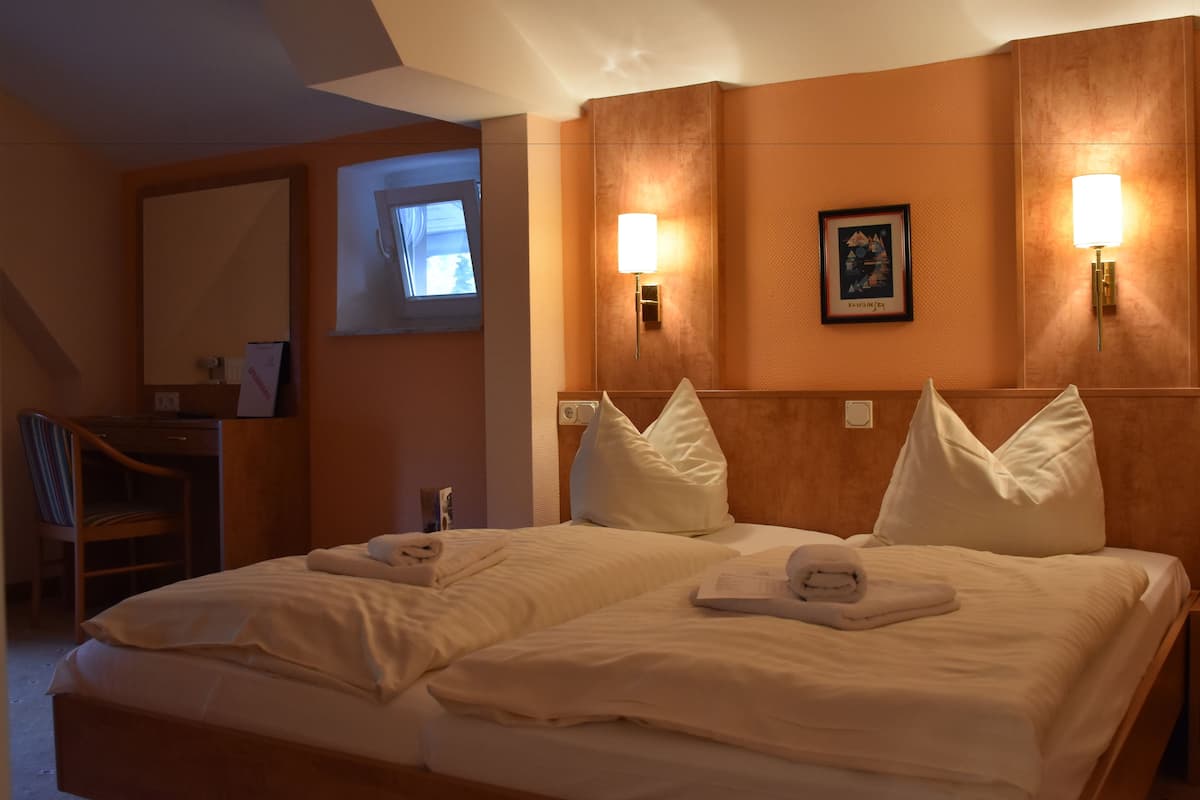 A hotel room with a large bed, two bedside lamps, a desk with a chair, and a framed picture on the wall.