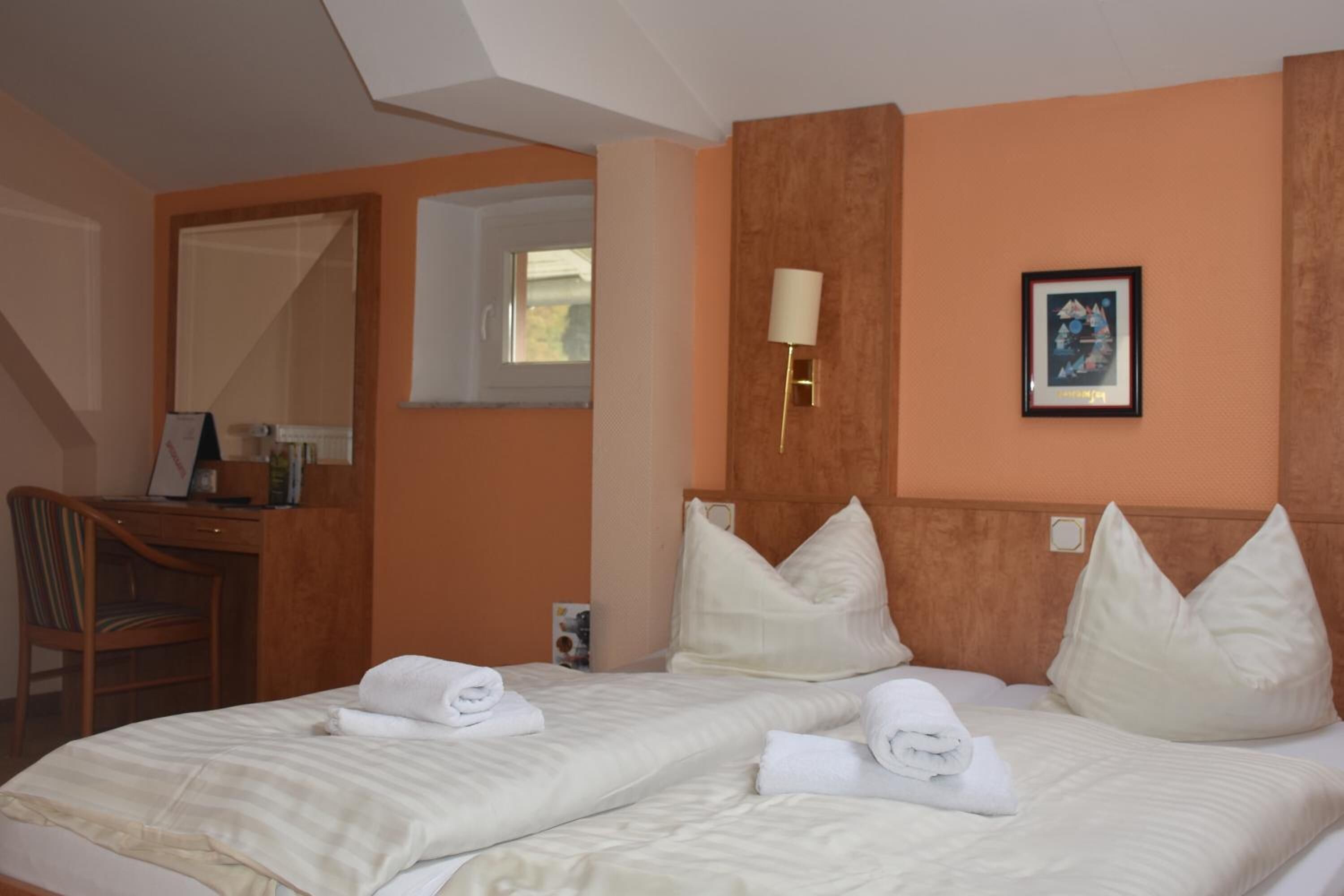 Habitació d'hotel amb dos llits, una taula, una cadira, una làmpada i un quadre al mur.