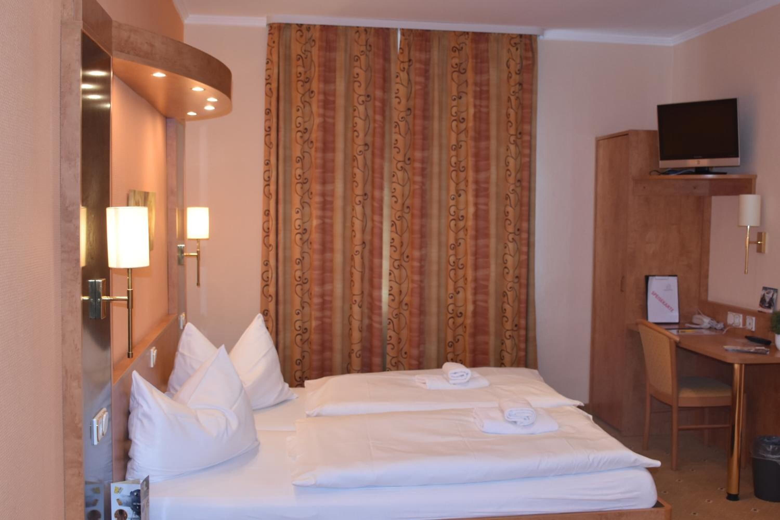 Een hotelkamer met een bed, een bureau, een televisie en een gordijn.