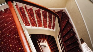 Una escalera de caracol con escalones alfombrados de rojo y barandillas blancas.