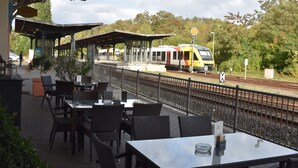 Un andén de estación de tren con asientos exteriores y un tren sobre las vías.