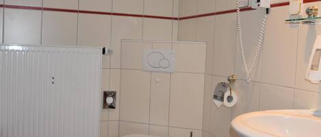 A bathroom with a toilet, a sink, a radiator, and a hairdryer mounted on the wall.