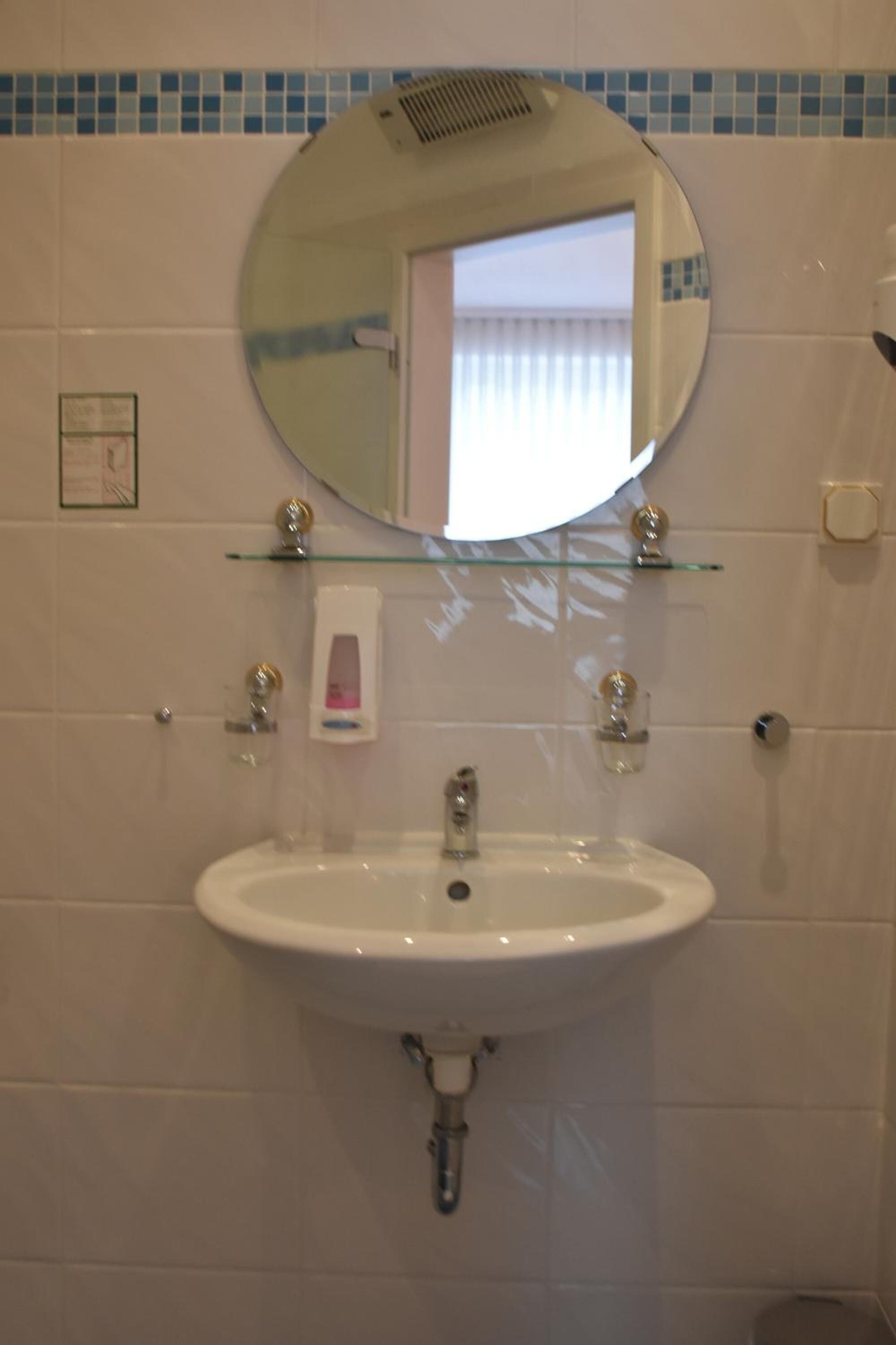 A bathroom with a white sink, a round mirror, and a glass shelf.