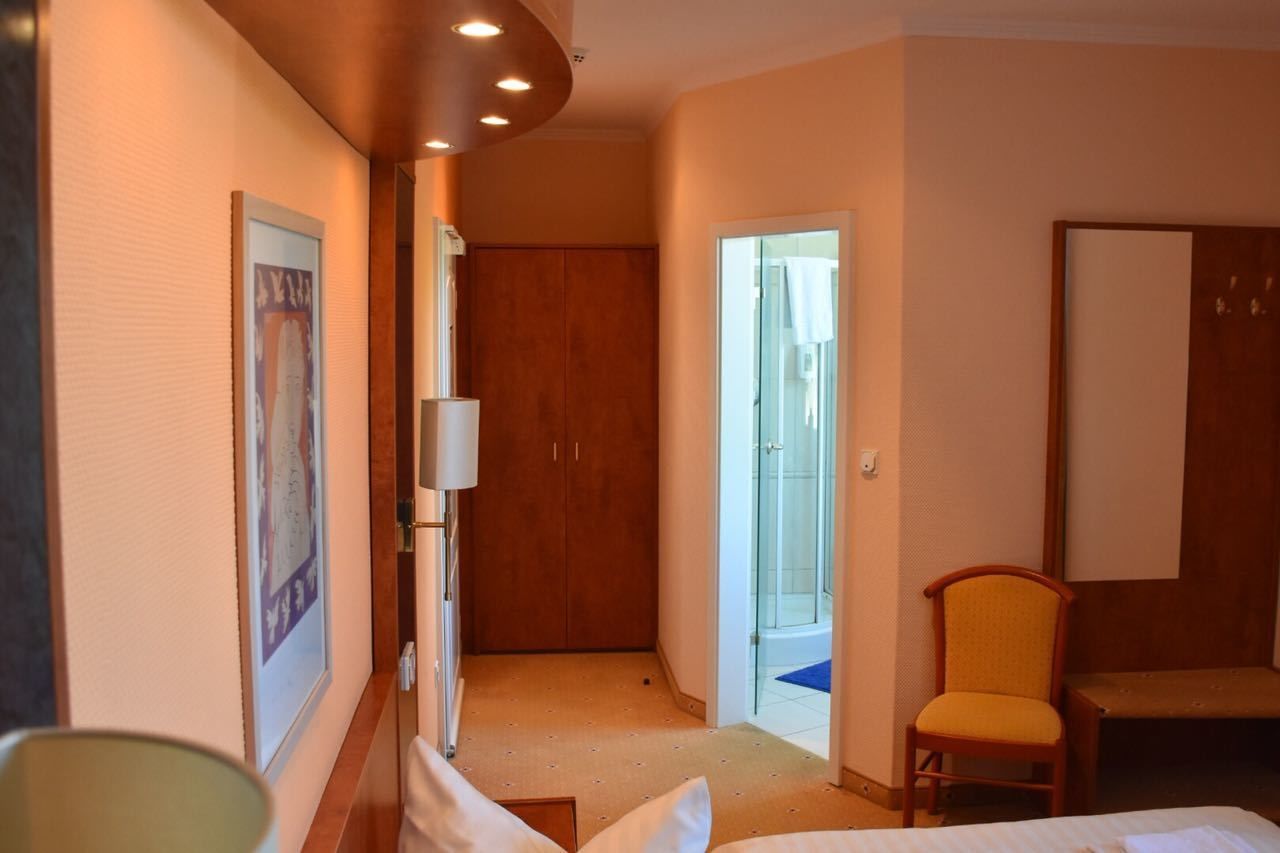 A hotel room with a bed, a chair, a wardrobe, and a shower area.