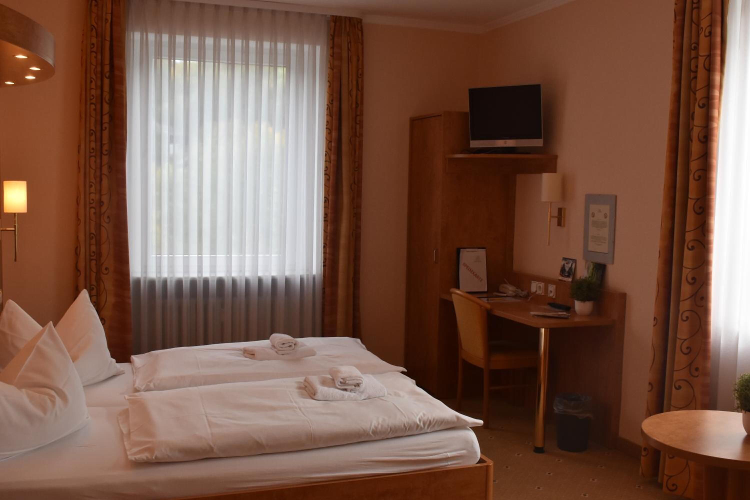 A hotel room with a bed, a desk, a television, and a small table.