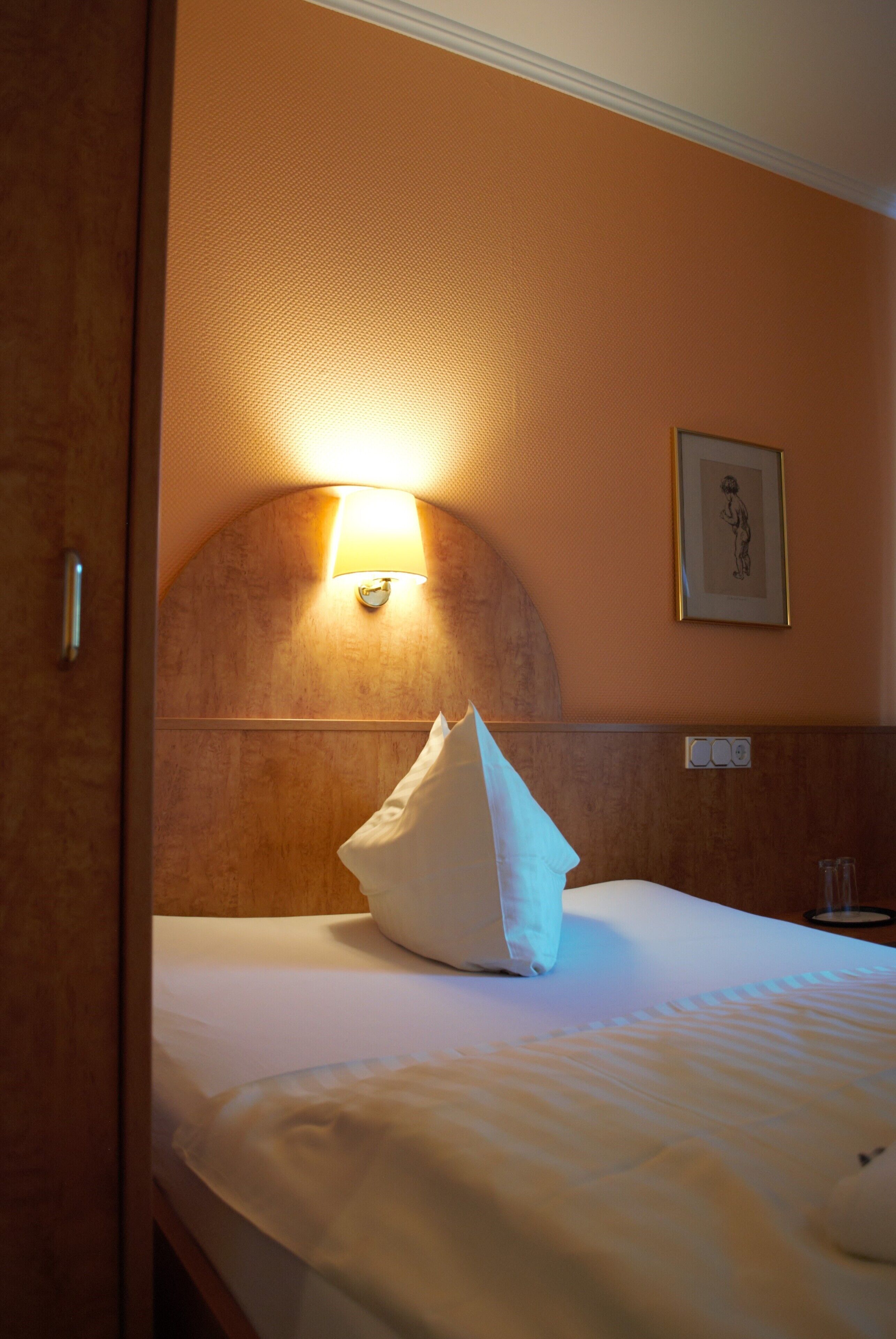 A hotel room with a bed, a wall-mounted lamp, and a framed picture on the wall.