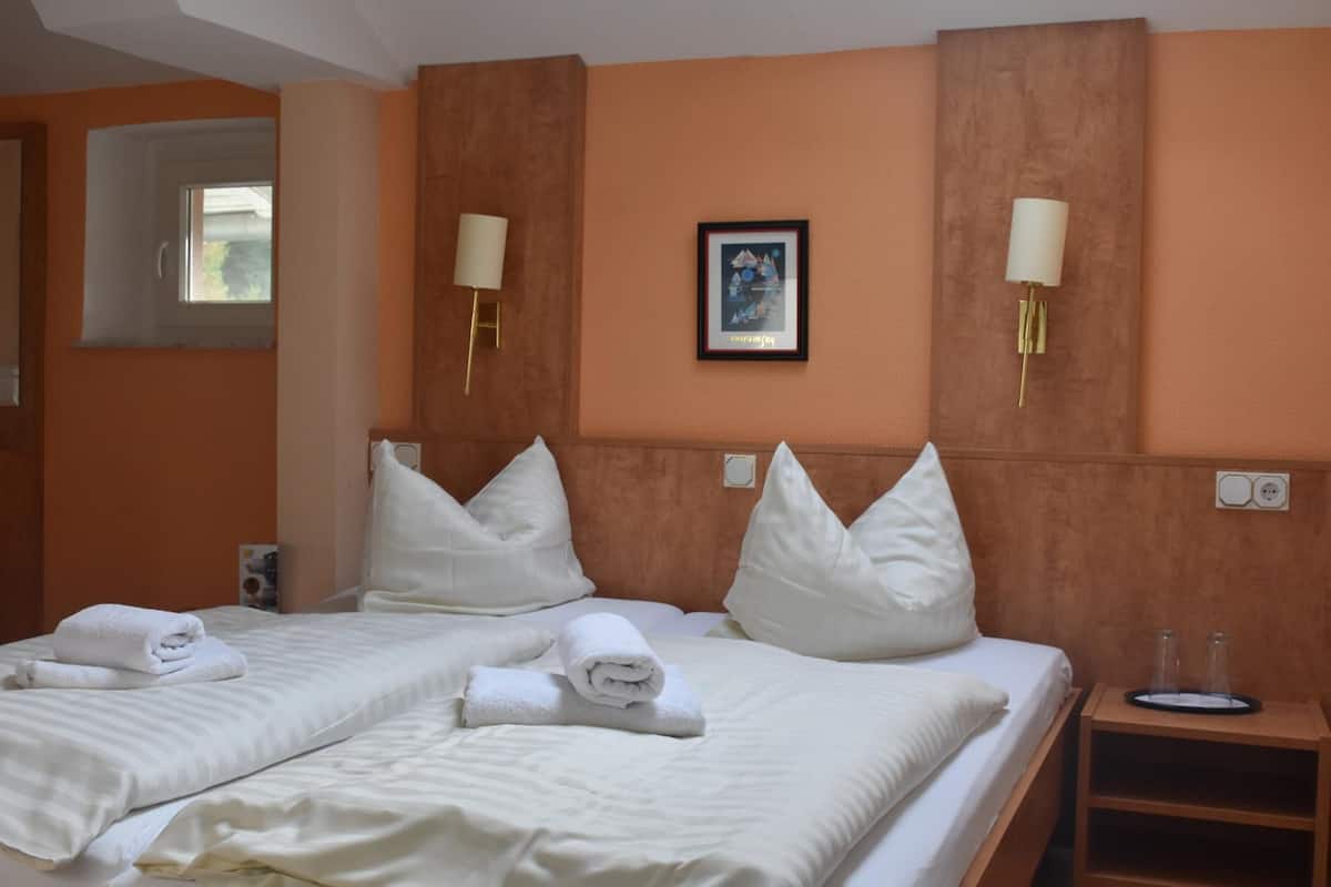 A hotel room with two beds, white linens, a framed picture on the wall, and a nightstand with glasses.