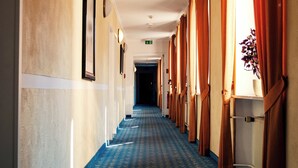 Un pasillo de hotel con alfombra estampada, cuadros enmarcados en las paredes y cortinas en las ventanas.