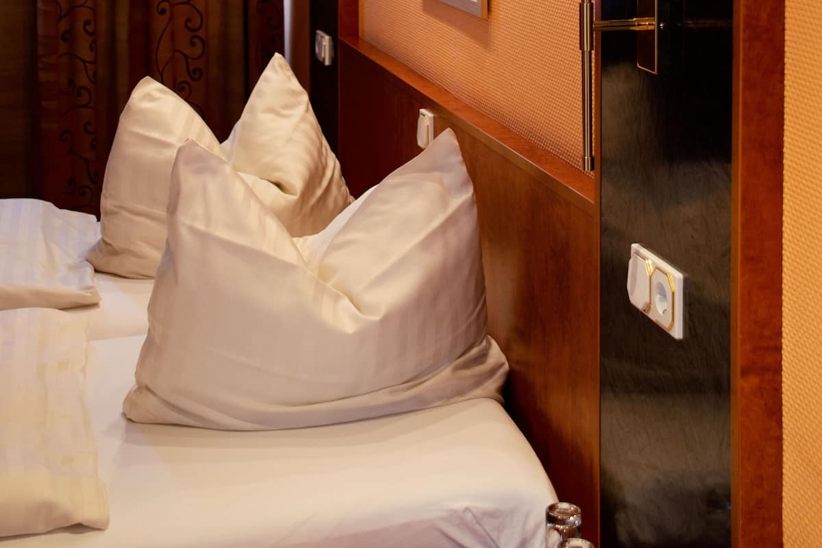 A hotel room with a bed, pillows, a wall-mounted lamp, and a framed picture.