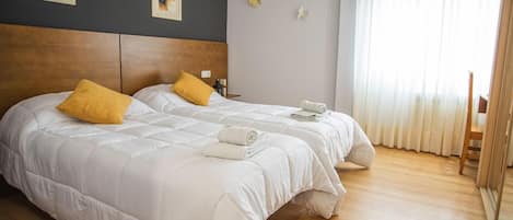 Una cama doble con almohadas blancas y amarillas, un cabecero de madera y una cama impecable con una toalla enrollada.