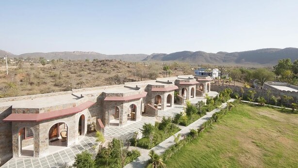 A row of stone buildings with red roofs, arched doorways, and a paved walkway. - Van Chhavi Resort (Rajgarh)