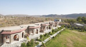 A row of stone buildings with red roofs, arched doorways, and a paved walkway. - Van Chhavi Resort (Rajgarh)