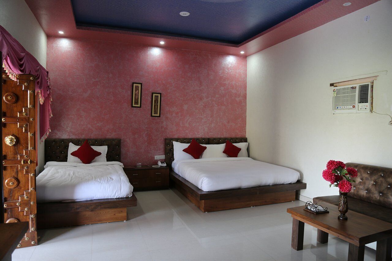 A bedroom with two beds, a wooden nightstand, a bedside table, a sofa, and a decorative vase.