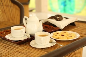 A breakfast setup with two cups of coffee, a teapot, a plate of cookies, and a tray on a woven table. - Van Chhavi Resort (Rajgarh)
