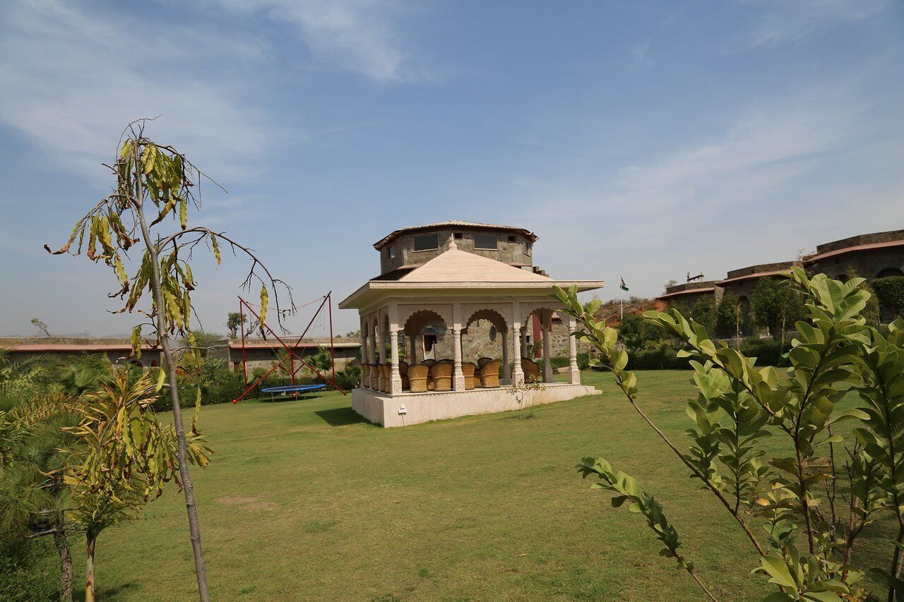 A traditional pavilion with a tiled roof and arches, surrounded by a well-maintained lawn and palm trees.