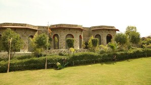 A stone building with arched windows and a well-maintained lawn. - Van Chhavi Resort (Rajgarh)