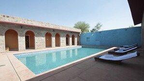 A swimming pool with lounge chairs and a stone building with arched doorways. - Van Chhavi Resort (Rajgarh)