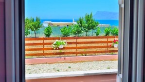 A view from a window overlooking a beach with a wooden fence, potted plants, and buildings in the background. - Eliana (Kissamos)
